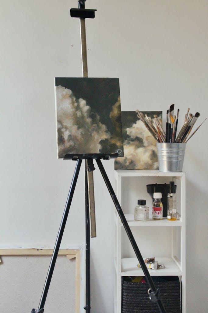 A creative indoor studio featuring cloud paintings, art supplies, and a tripod easel.